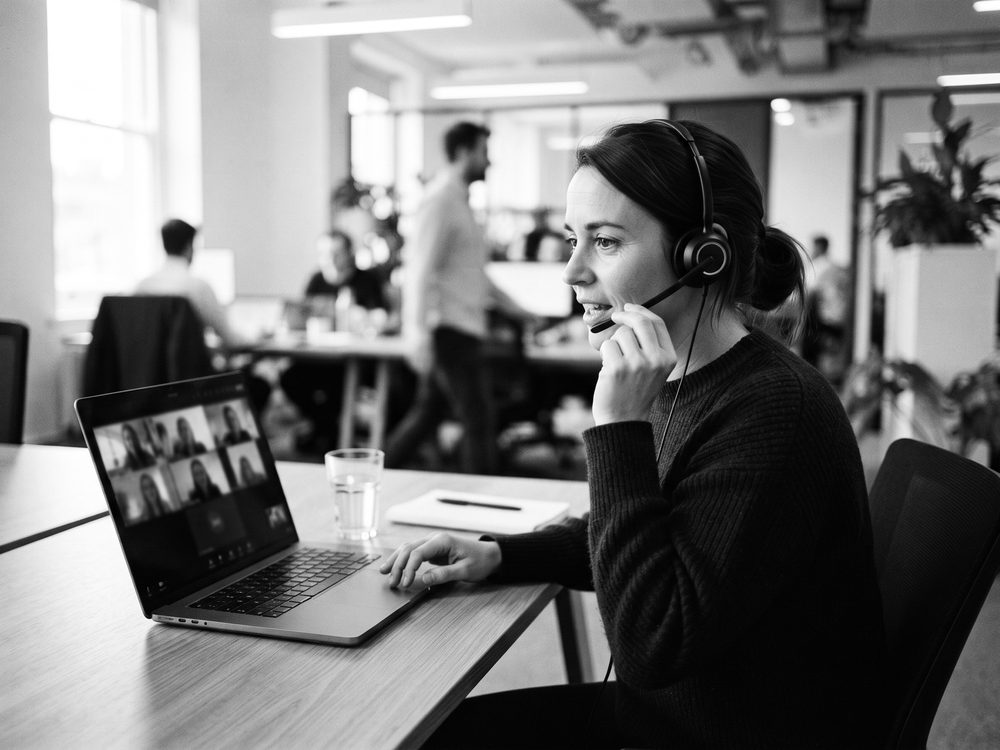 Frau mit Headset vor einem Laptop mit mehreren Videokacheln
